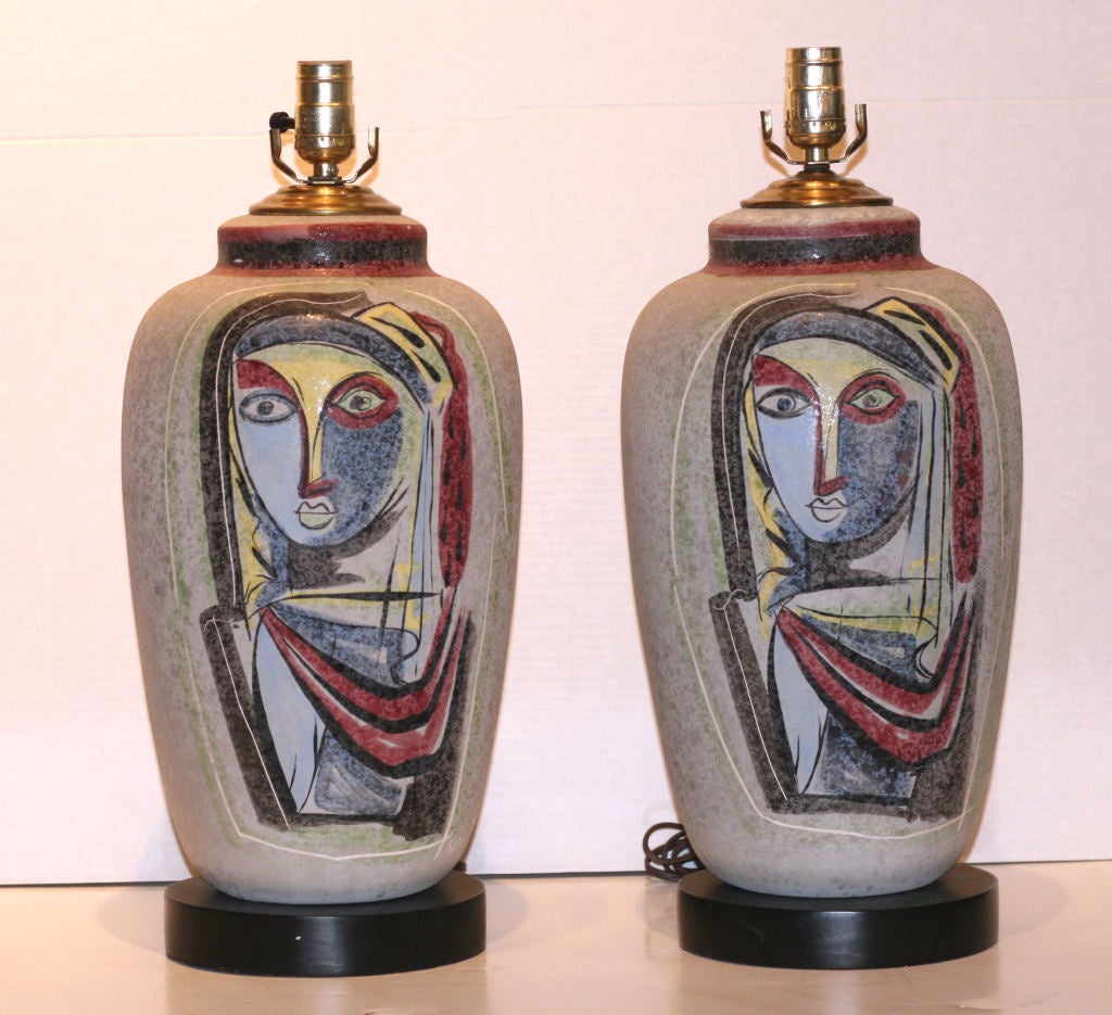 This large and beautiful pair of painted ceramic table lamps by Tye of California exhibit Picasso-like graphics of women's faces in abstract and colorful design. In excellent condition, they are ready to adorn any high end Mid Century interior.