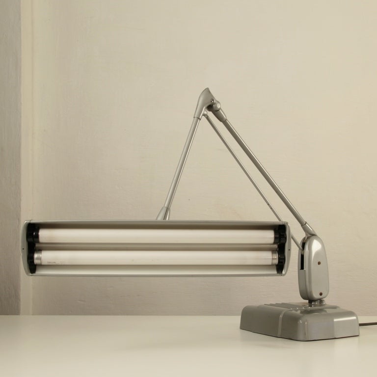 Old industrial metal table/desk lamp with a floating adjustable arm.

Highly decorative.

Uses two 15-watt fluorescents (F15T8) to provide abundant light over a large work.

Very good vintage condition.


