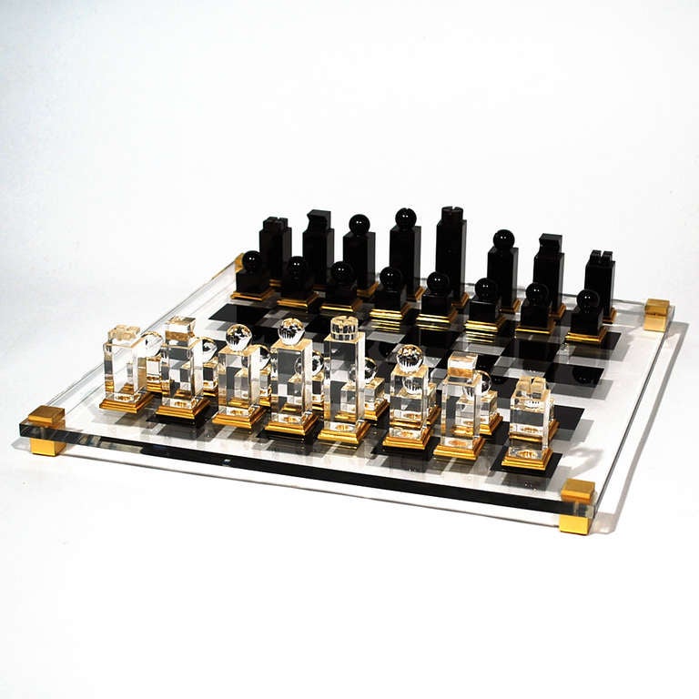 Elegant Lucite chess set with gold leaf accents. Designed by Michel Dumas, circa 1970s. The black and clear lucite figures sit atop a glass chess board.