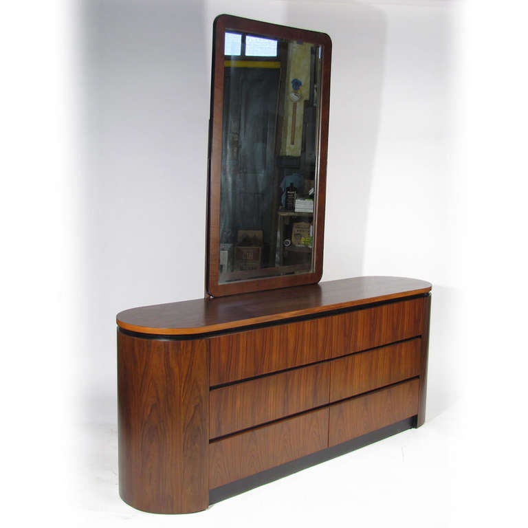 Unusual Art Deco influenced oval pill form six drawer dresser. Beautiful rosewood drawer fronts, curved sides, and top, with satin black spacers and base front. Matching mirror with black metal border. Mirror 29