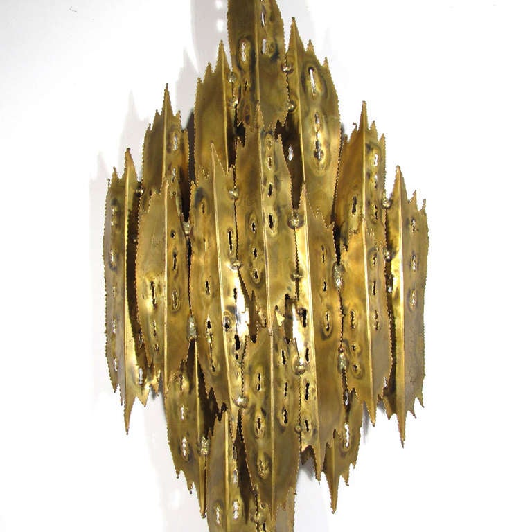 Rare brutalist torch cut wall sconce designed by T. A. Greene for Feldman. Long folds of brass with polychrome accents hide a porcelain light source located on backside.

Rewired. Overall excellent condition.