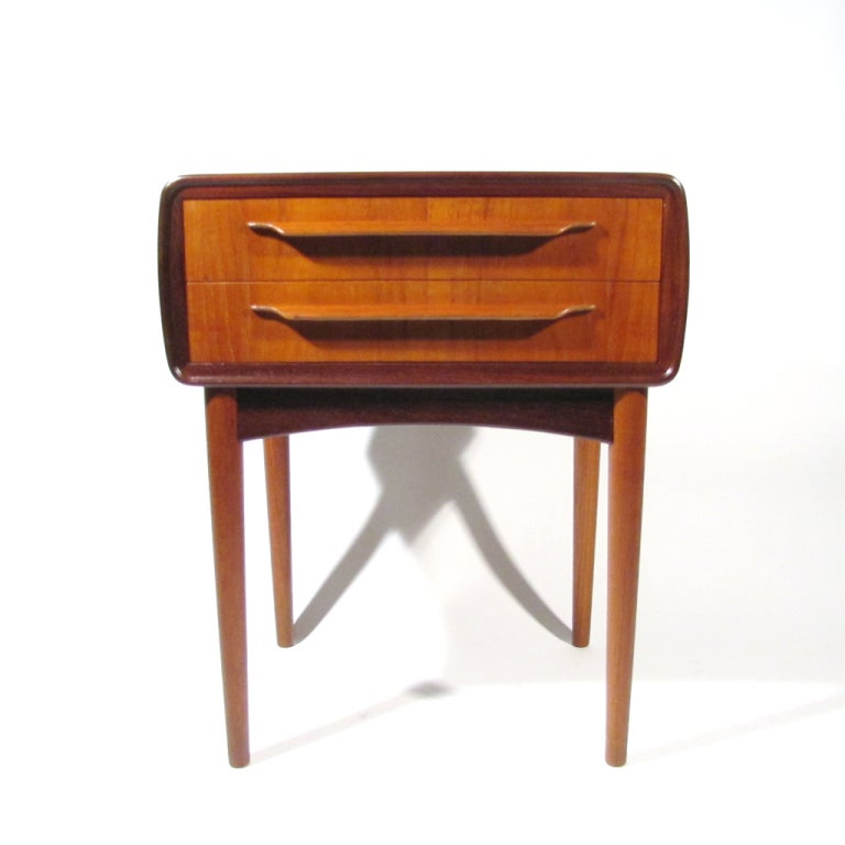 Diminutive Danish teak Johannes Andersen two drawer table with rosewood border. One sheet of beautiful teak extends across top and down both sides.Teak curl pulls with honey beech interior. Unusual little gem.

Impeccably refinished. Please call