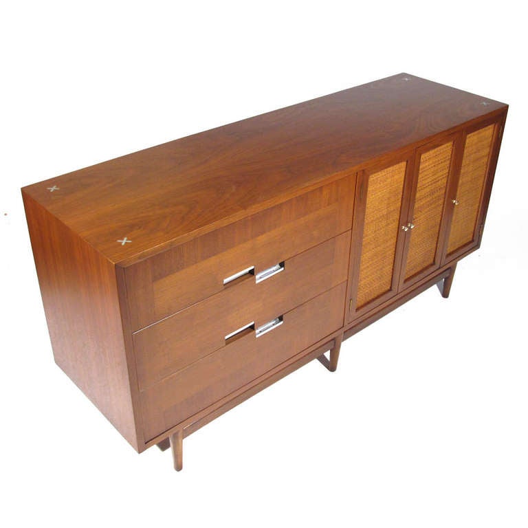 American Mid-Century walnut sideboard. Three drawers on left with three canned doors on right revealing shelved compartment. All pulls original, polished brass pulls on doors and nickel on drawers. We will plate either to match the other at no