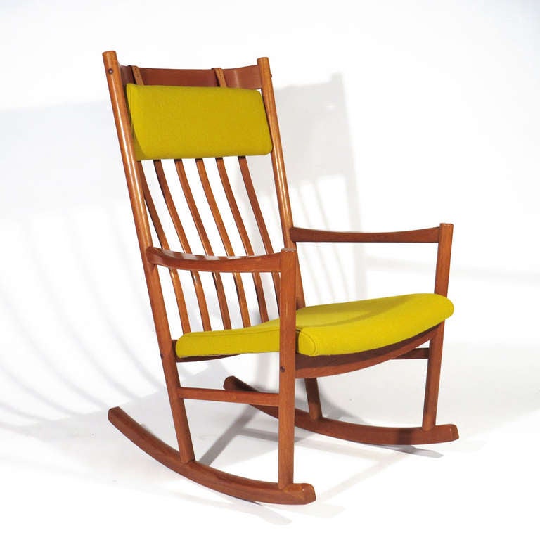 Hans Wegner rocking chair in teak. Upholstered in saffron Hallingdal. Head cushion adjusts with openings in leather strap attaching to brass button.

Newly upholstered. Immaculate restored condition.