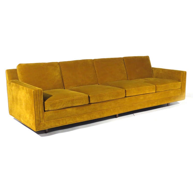 Sleek Harvey Probber four seat sofa upholstered in deep burnt gold. Cushions wrapped in down. Walnut legs. Harvey Probber labels affixed to underside.