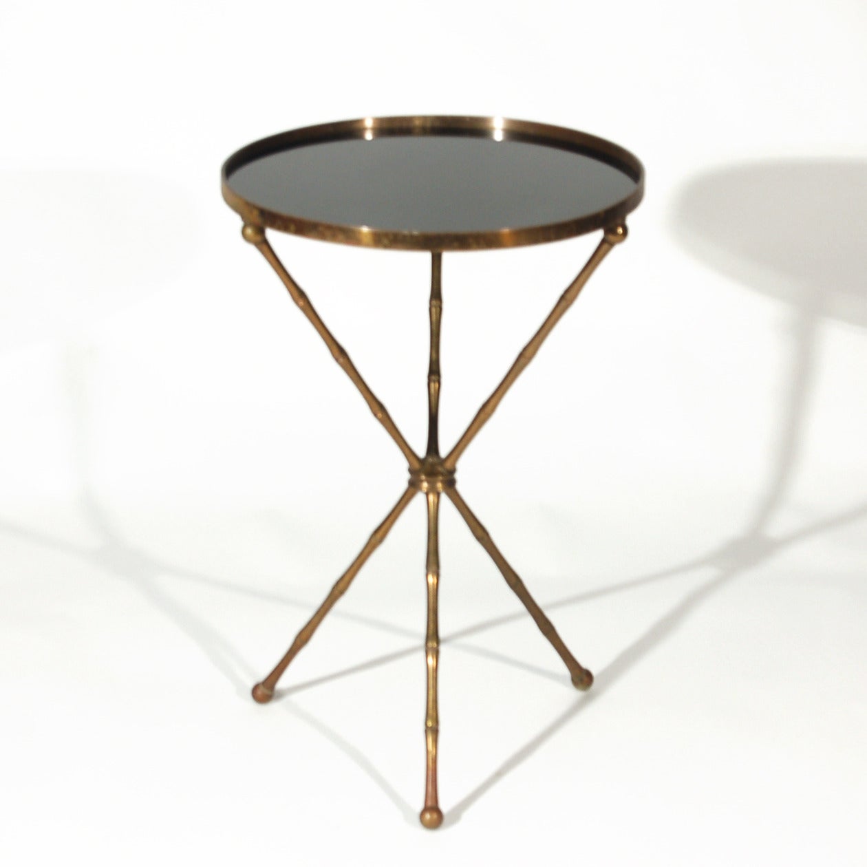 A beautiful vintage brass tripod form table with faux bamboo legs. Very much in the Maison Bagues style -could actually be Bagues -we can't be sure. The table features black Carrara Vitrolite glass. We have left the wonderful patina as-is. This