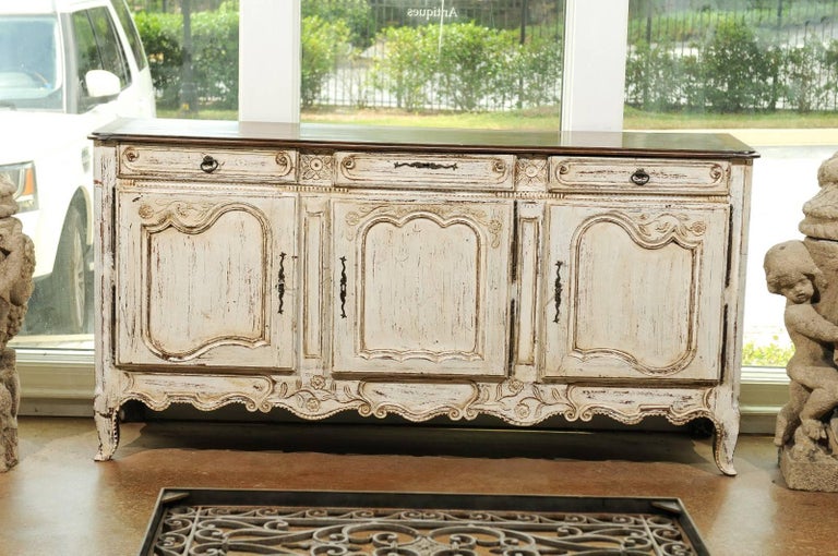 A French Louis XV style painted wood enfilade from the 19th century with three-drawers over three doors. This French long buffet features a rectangular wooden top with beveled edges sitting over an off-white painted and carved body. Three dovetailed