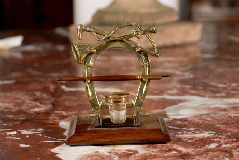 An English Edwardian period inkwell from the early 20th century, with brass equestrian motifs and wooden base. Born in the early years of Queen Victoria's son Edward VII's reign, this elegant piece features a central inkwell, accentuated in the back