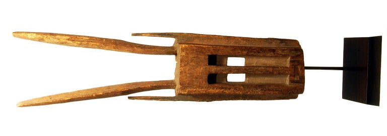 A large and graphic abstract angular light brown wood mask; with a high forehead with raised middle ridge merging into a triangular nose, flanked by open worked rectangular eyes, a prominent mouth below,


The mask 
