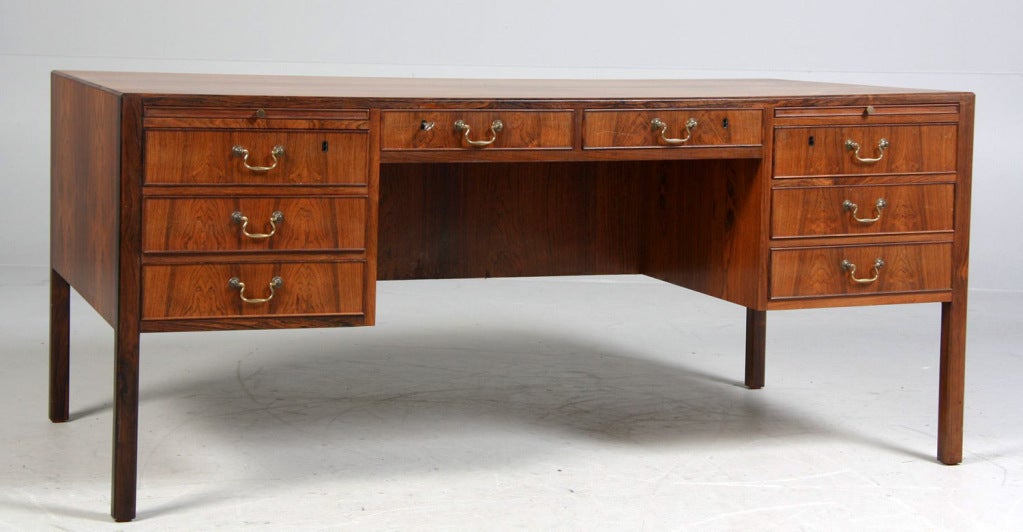 Very Rare Jacob Kaer. Free-standing  rosewood desk.
Made by cabinetmakers Christensen & Larsen. 1950's.
Table top with chamfered edges.
Front with eight drawers and two sliding trays
Brass drawer handles.
Reverse with two compartments, two