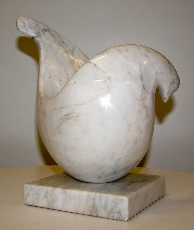 A white Carrara marble sculpture of a stylized dove resting on a marble base.  The sculpture rotates 360 degrees on the base.  This sculpture echoes the style of sculptors Jean Arp and Constantin Brancusi.