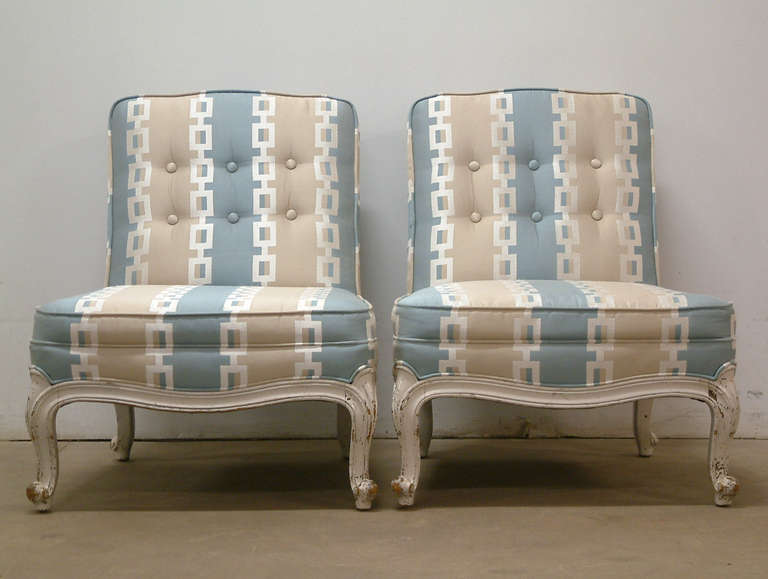 A very elegant pair of carved wood French provincial style boudoir chairs manufactured by Drexel. The chairs are painted an eggshell white with a distressed finish probably done in the 1960s and were reupholstered in an Anna French cotton twill