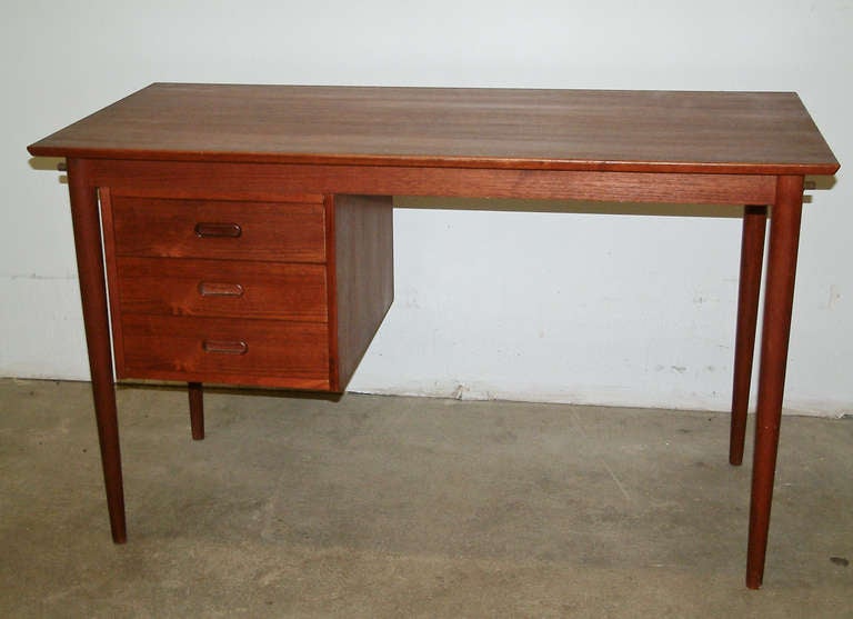 A small scale teak desk with a three drawer cabinet that slides along a wooden track to become a left or right hand unit.  Signed H. Sigh & Son Denmark with the maker's logo on the underside.