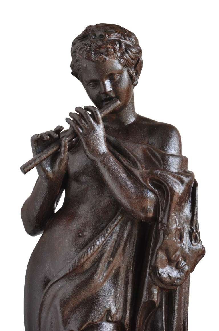 After the antique: a Val D'Osne Foundry cast iron figure the Faun with Pipes, French, circa 1870, standing naked except for a fig leaf and playing a flute, next to a pedestal draped with a lion skin, on rectangular base. The Faun was certainly in