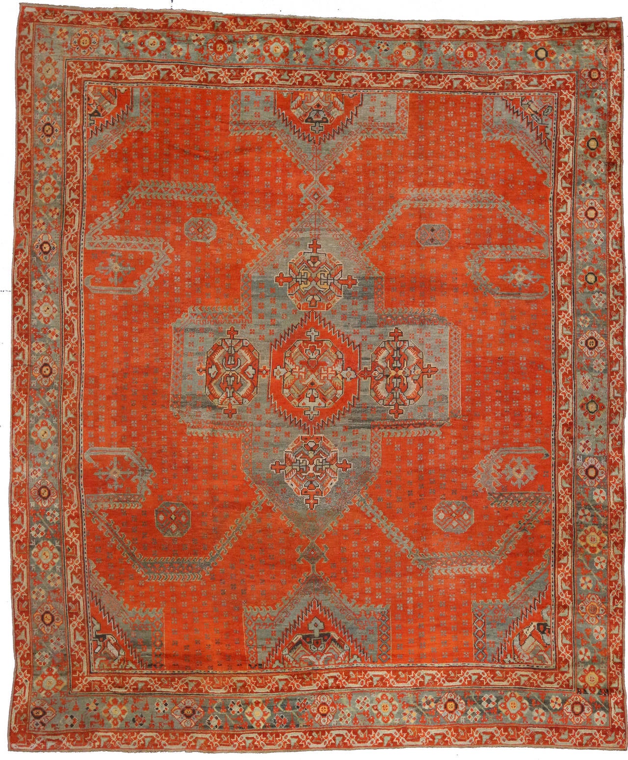 This Mid-Century Modern styled antique Turkish Oushak features a modern center medallion with an overall geometric pattern. The background is a vibrant orange and has a powder blue border and center medallion. Warm up nearly any space with this