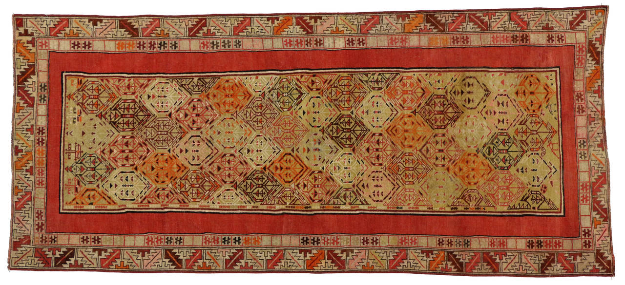 This vibrant antique Oushak (Ushak) runner features an allover repetitive field of hexagons. The solid red bolder and geometric border create a dense abstract pattern as they cross the vibrant background of this antique Turkish carpet runner. The