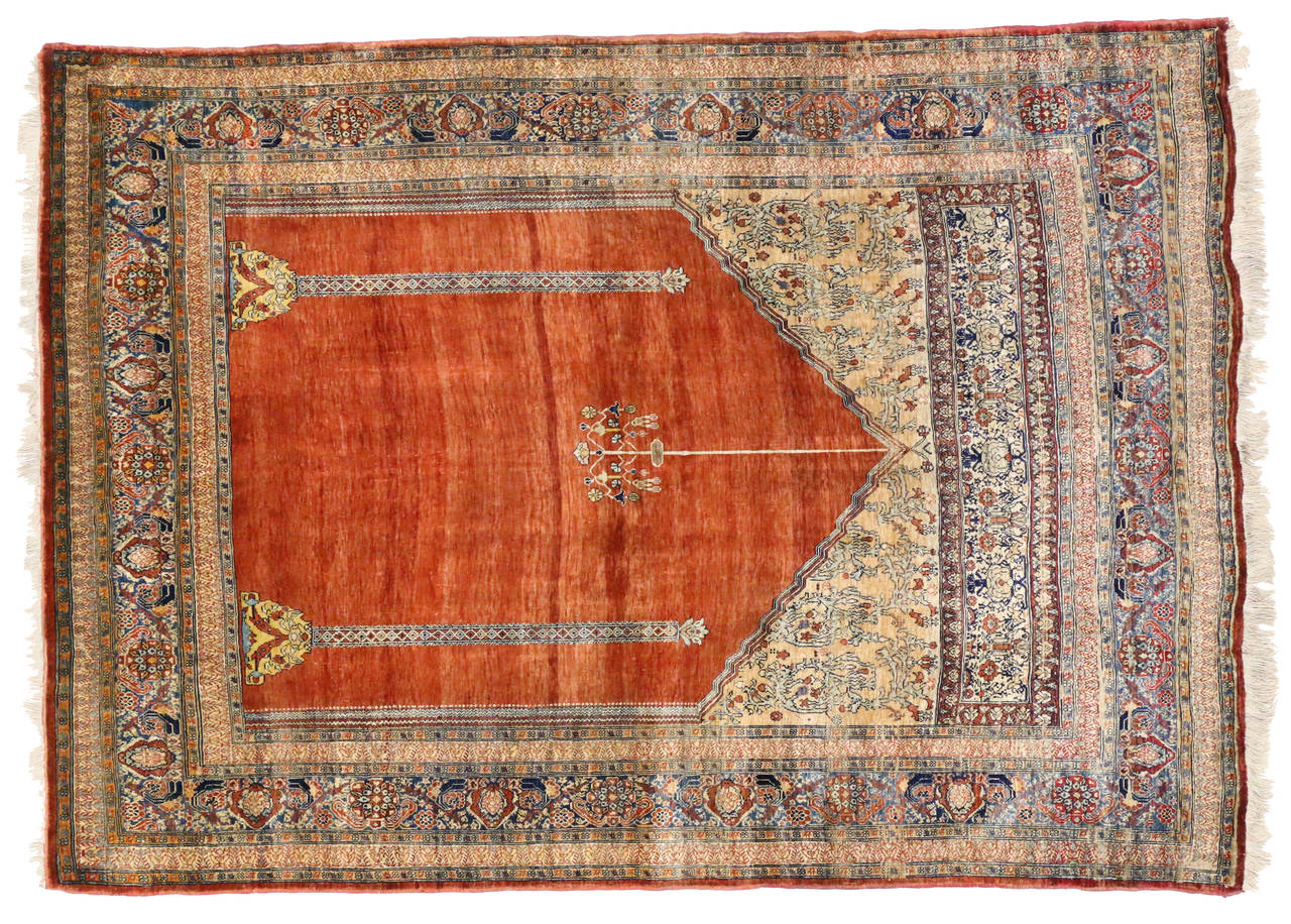Haji Jalili was a well-known master craftsman from Marand, a small town northwest of Tabriz, Iran. This antique silk Tabriz prayer rug features two stylized columns and delicate chandelier that Stand gracefully against the Vermillion red abrashed