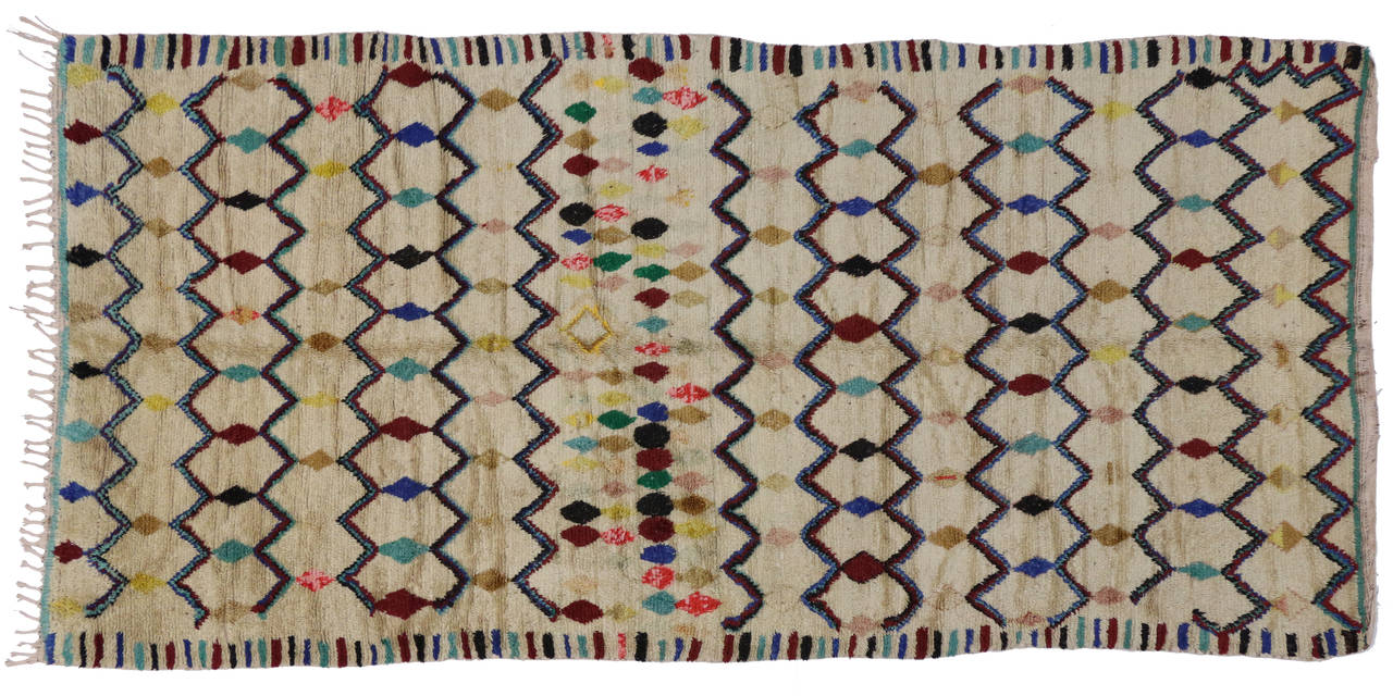 The Moroccan carpets and rugs are part of North Africa's renowned indigenous tribe weaving. This vintage Moroccan rug features an all-over pattern of diamonds and zigzag lines creating a harlequin like design that is enclosed by a colorful border of