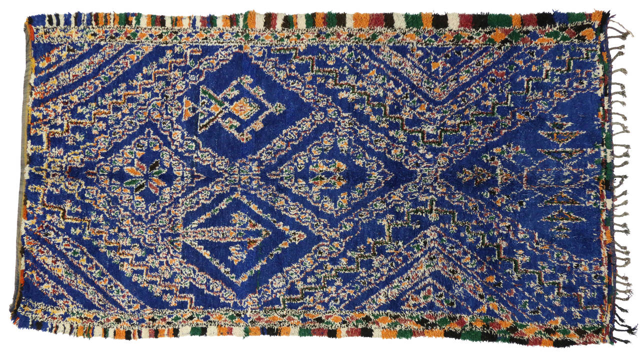 This beautiful vintage Moroccan carpet was made by the Beni Ouarain (Beni Ourain) tribes in Morocco's Atlas Mountains. The palette consists predominantly of cobalt blue with multicolored hues of ivory, rust, orange, yellow, green and small flecks of