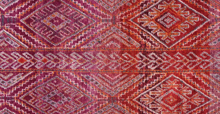 This beautiful vintage Moroccan rug has an all over diamond pattern with varying hues of red, purple, and orange. The white lines on this piece accentuate the pattern and border.