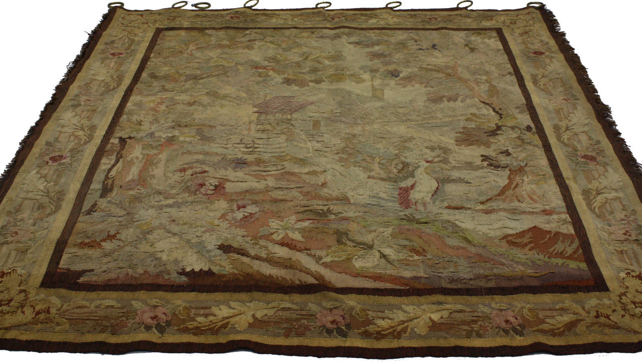 This spectacular antique French tapestry was made from handwoven wool in the late 19th century, circa 1880. The meticulous details define the idyllic French countryside scene. Two trees frame the left and right sides with a cottage nestled between a