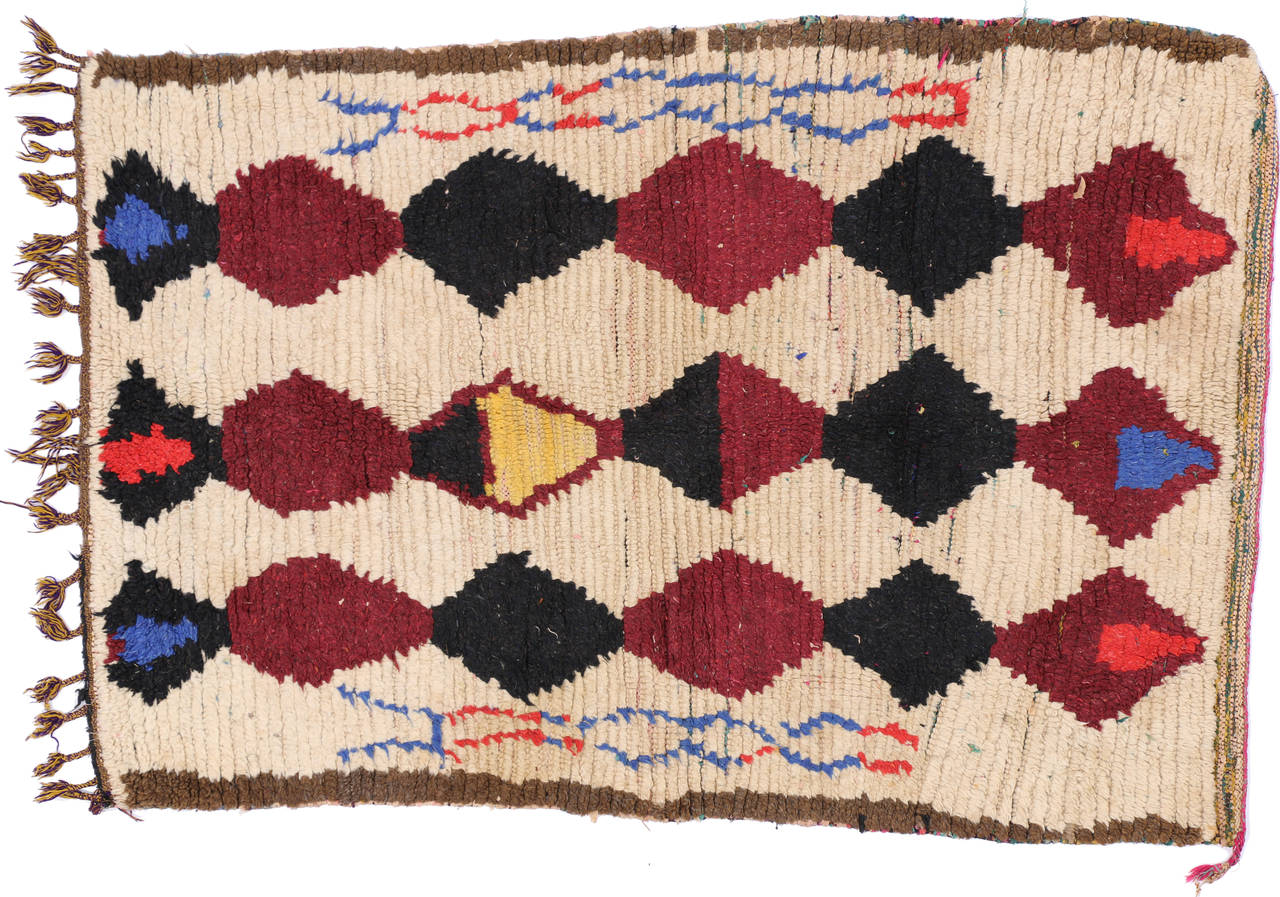The Moroccan carpets and rugs are part of North Africa's renowned indigenous tribe weaving. This unique vintage Moroccan rug features three rows of stacked diamonds in a colorful palette of maroon, black, red, blue and yellow on a creamy beige