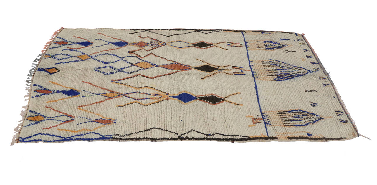 Transform your interior space into a Moroccan delight with this vintage Moroccan carpet from the Azilal region. Orange hues of rust, salmon peach combined with dark brown and blue contrast beautifully on the light colored field. With the whimsical