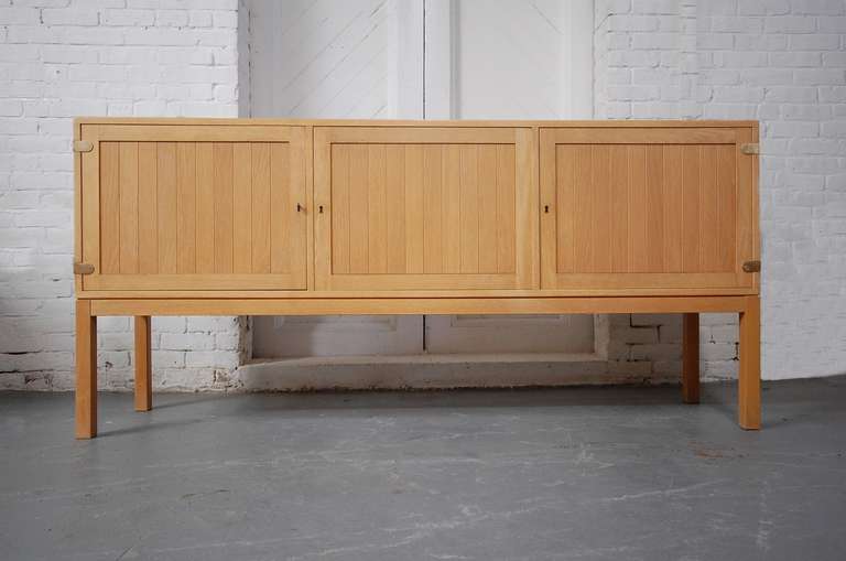 Cabinet in oak and brass by Børge Mogensen, designed circa 1958. Produced by P. Lauritzen of Denmark. Solid brass hinges and escutcheons.Three compartments. Two having adjustable shelves, the third having two drawers.

We offer free delivery on