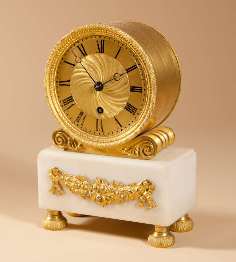 A drum-shaped Regency period mantel clock with an 8-day timepiece movement by David & William Morice, London.  The gilt face with engine turned center matting, matched blued steel hands and resting on a  scrolled plinth above a white marble base