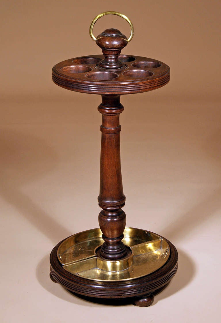 English 19th Century Mahogany Stick or Umbrella Stand: with a brass loop handle set within the turned finial above a circular pierced stick holder with six circular openings and enriched with a reeded edge; supported on a turned standard and resting