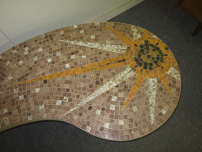 LOVELY KIDNEY SHAPED TILE TOP COFFEE TABLE.   I LOVE THE SUNBURST DESIGN ON ONE SIDE WITH THE SINGLE DOVE ON THE OTHER SIDE.  THERE IS A BAND OF BRASS AROUND THE TABLE WITH BRASS COLORED LEGS.  ALL THE TILES ARE PRESENT AND IS REALLY QUITE NICE AND