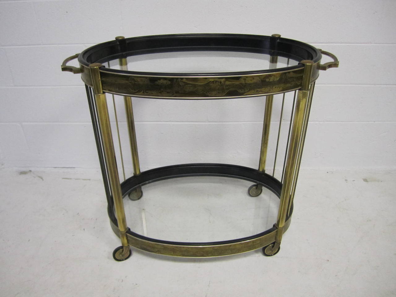 Brass oval bar cart by Bernhard Rohne for Mastercraft.  Black lacquered and acid etched brass wrapped oval bar cart by Mastercraft. Patinated brass legs and polished brass rods support the glass bottomed serving areas, which are wrapped in Bernhard