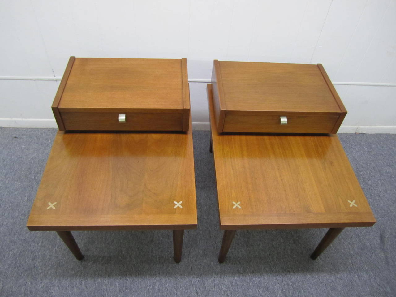 Handsome pair of American of Martinsville walnut step end tables.  Manufactured by American of Martinsville - in Martinsville, VA. Extremely well constructed and sturdy. Upper section with dove-tailed drawer. Cross inlaid motifs on corners.