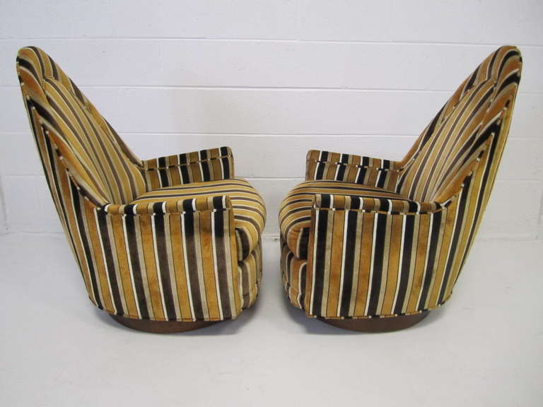 A pair of sculptural, fully upholstered and highly comfortable lounge chairs upholstered in it's original striped velvet fabric. Rising from a walnut disk base, these diminutive chairs have a high degree of mobility, tilting and swiveling with great