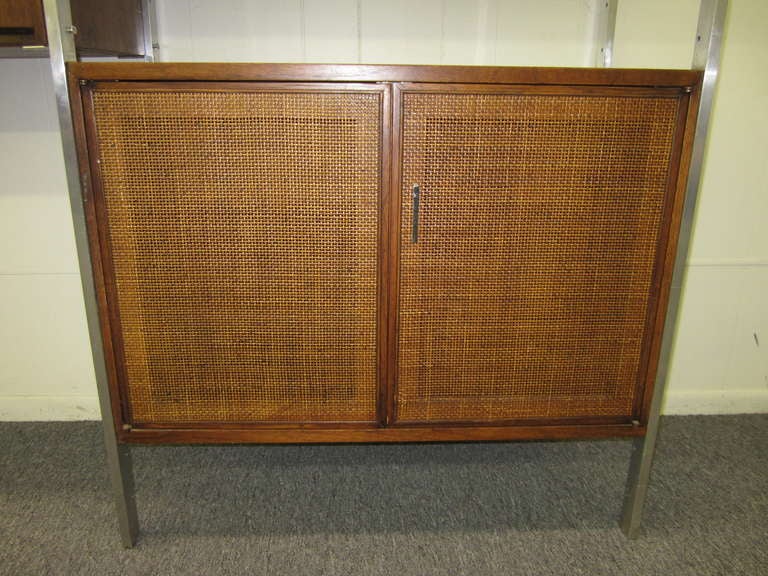 Wonderful Milo Baughman style three bay walnut and caned wall unit. The upright poles are solid aluminum along with the pulls. One cabinet has a lovely caned front with a single shelf. The middle cabinet is a pull down desk with some cubbies and a