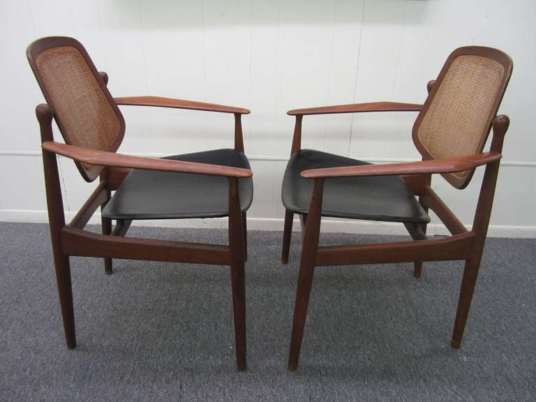 WONDERFUL PAIR OF DANISH MODERN TEAK ARNE VODDER ARM CHAIRS.  THE CHAIRS RETAIN THEIR ORIGINAL WARM HONEY FINISH, CANED SWIVEL BACKS AND BLACK LEATHER SEATS. THEY ARE SIGNED WITH A FRANCE AND DAVERKOSEN MEDALLION ON THE UNDERSIDE.