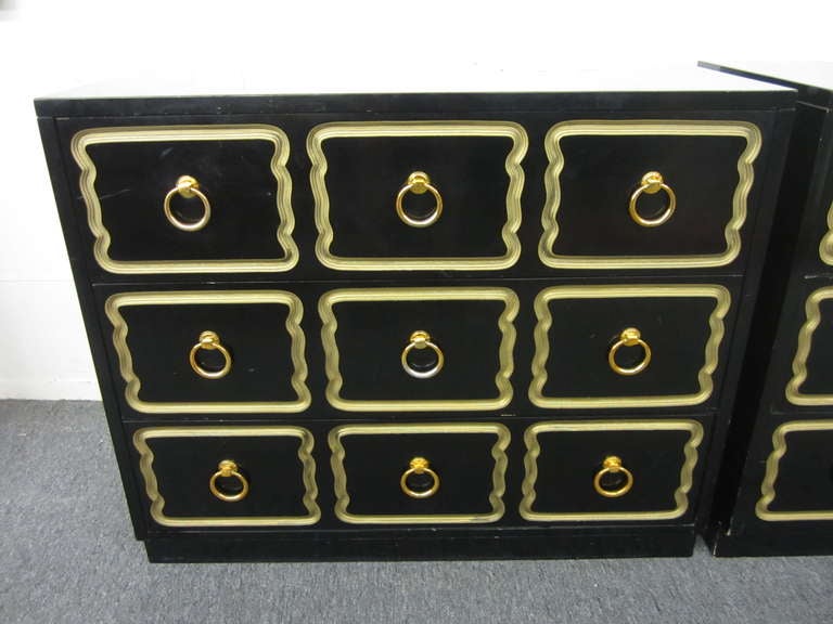 Pair of Dorothy Draper Espana rectangular chests with new black lacquer finish, features three drawers decorated with a repeated routed pattern. Large brass ring pulls adorn the centers of the nine wavy gold rimmed shapes. The low luster black