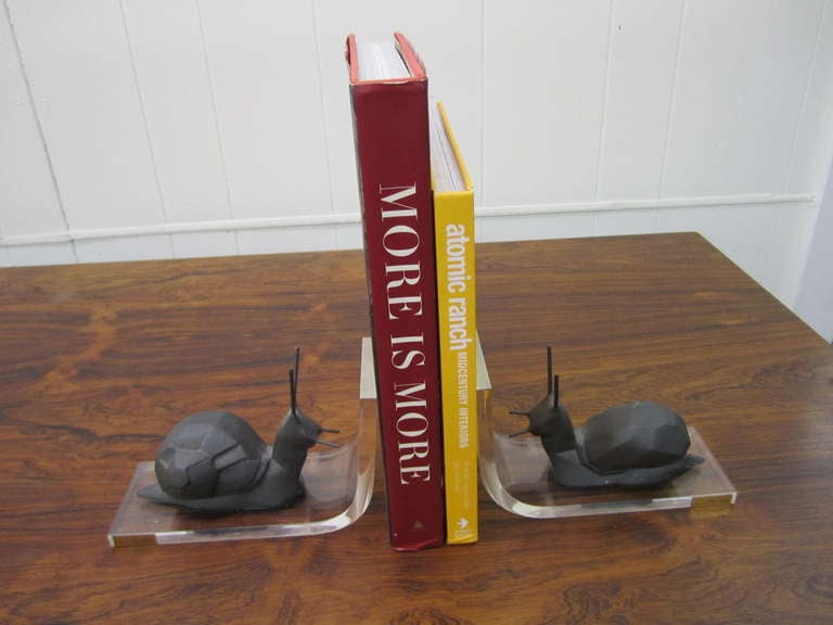 Whimsical pair of lucite and cast iron bookends. The snails are wonderfully sculpted in the cubism style and have a almost sandy texture.  I love the stylized textured snails against the smooth clear lucite.  There is a small brass plate signed 