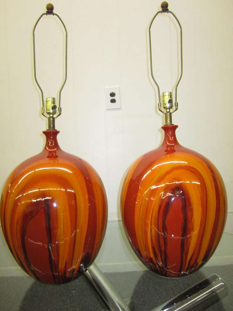Amazing pair of huge bulbous orange drip glazed lamps.  You will love the gorgeous array of sunrise orange colors along with the sheer size.  These lamps are in fantastic vintage condition and retain their original harps with walnut finials