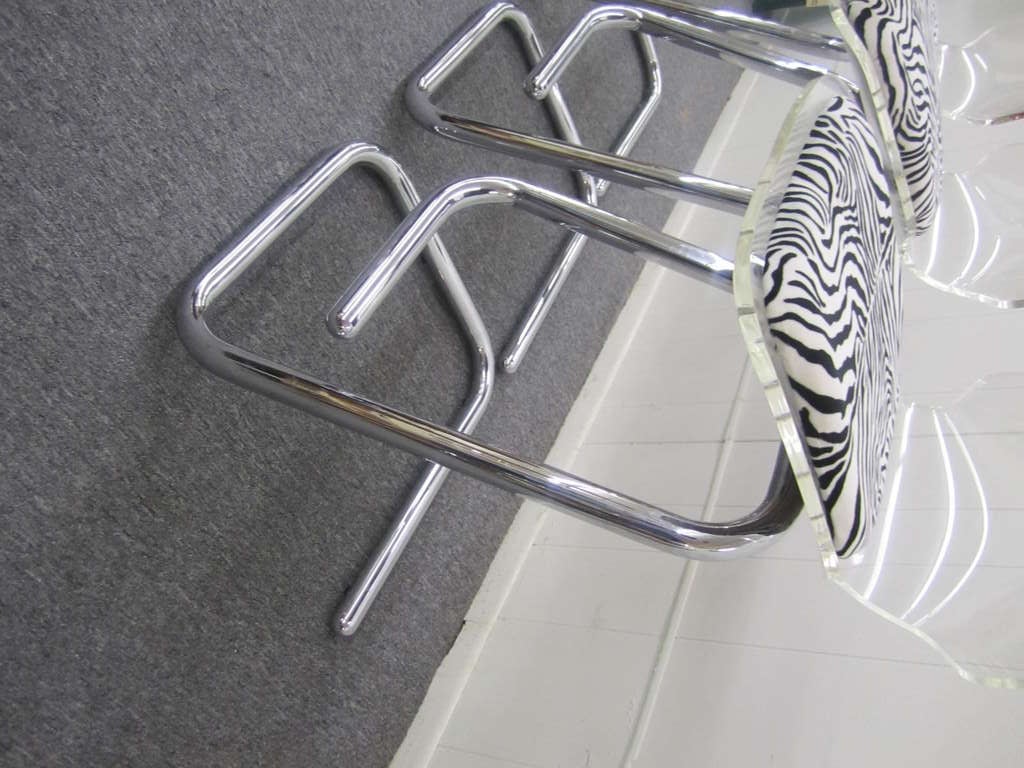 Glamorous set of three Lucite and chrome bar stools. This set of three has sexy, chunky, sculptural chrome legs and are upholstered in zebra velvet. The Lucite is also nice and thick and well sculpted.