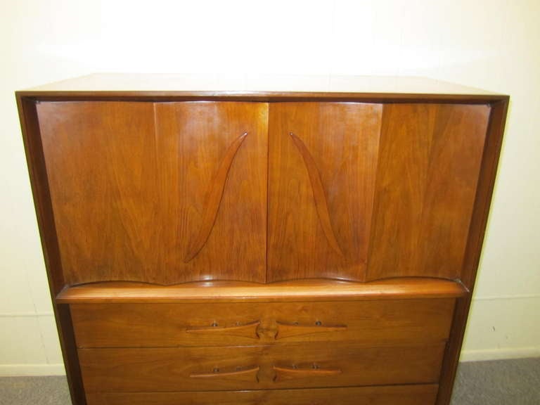 Lovely American modern walnut tall dresser. Very interesting details with large sculptural pulls and nicely carved legs. I have the matching night stands and credenza if your looking for additional pieces. Wonderful scalloped front doors open to
