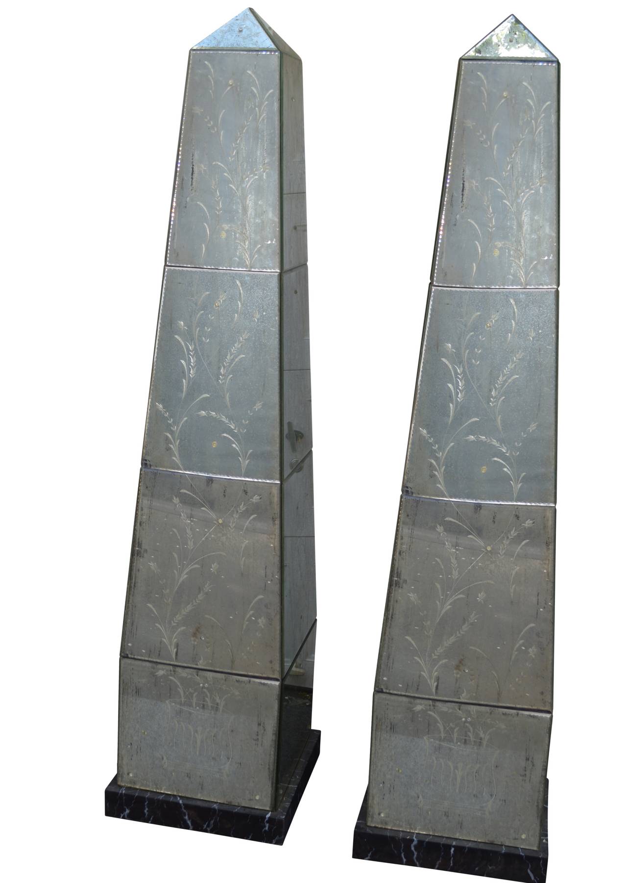A stunning pair of Venetian-style mirror-glass obelisks on faux marbeled wooden base. 

Glass has simple flower decorations etched in Murano style on each foliated glass pane.

Designed by American designer couple and made in Italy.

See 2007