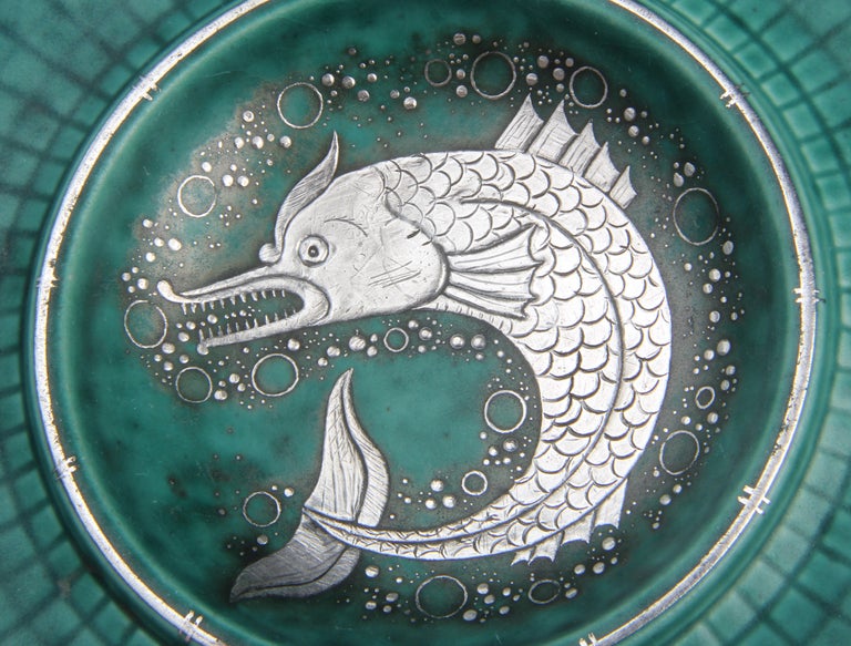 This is a beautiful Swedish Gustavsberg plate from the Argenta line.  It is very well drawn and  depicts an almost mythical looking fish created in amazing detail. The sterling silver work is amazing.
It is marked on the back , Made In Sweden,