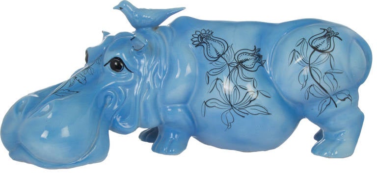 This is a playful ceramic piece depicting a blue hippo with a painted floral motif.