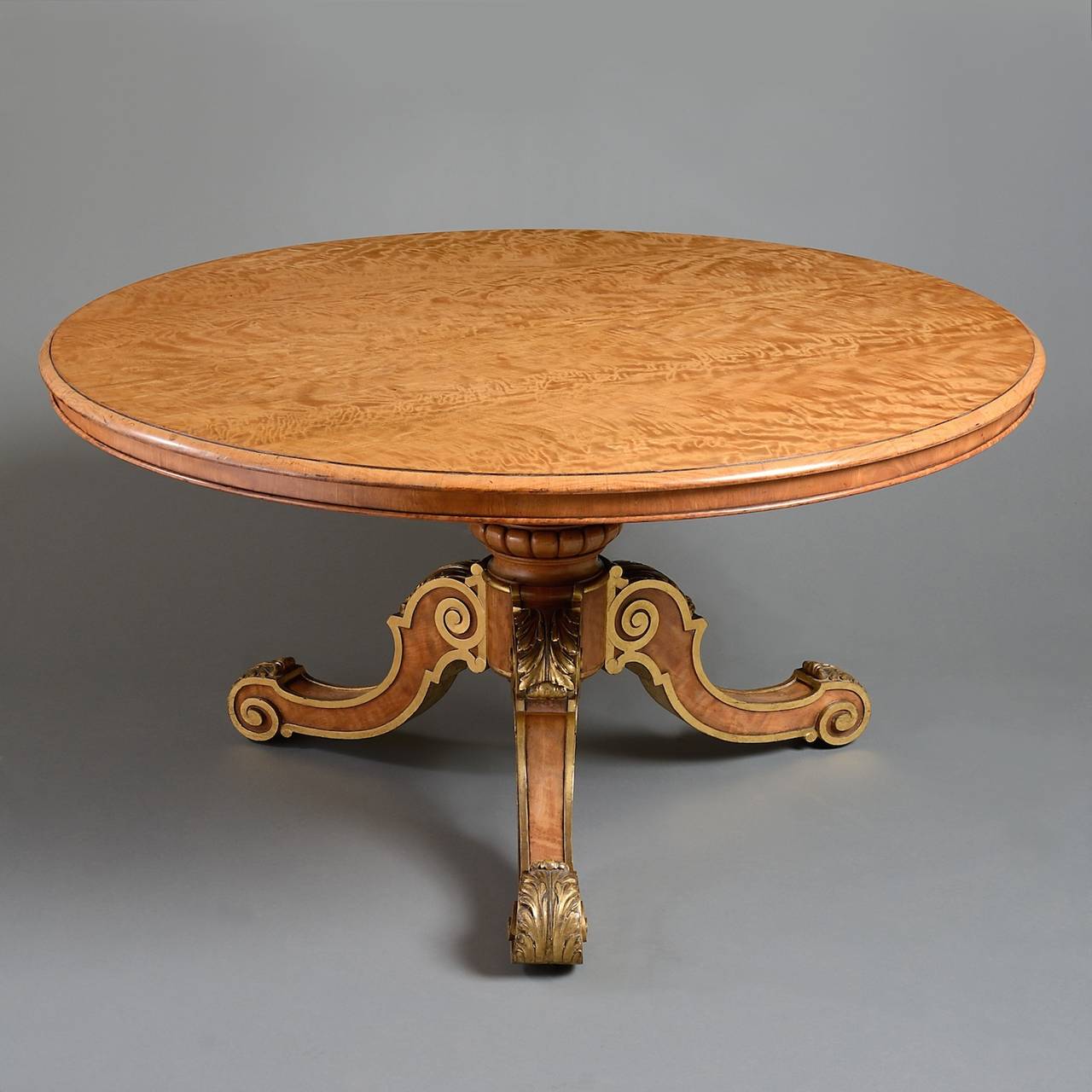 A fine early Victorian parcel-gilt satinwood center table attributed to Holland & Sons, circa 1860.
With figured circular tilt-top on a baluster stem and tripod base carved with foliage, in exceptional condition, retaining all its original