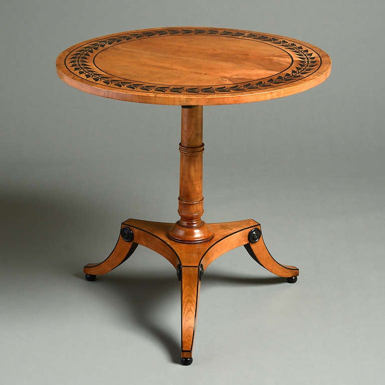 A regency ebony-inlaid cherry wood centre table attributed to George Bullock, circa 1820.
The circular tilt-top with broad stylised foliate inlaid band within a mulberry crossbanding.