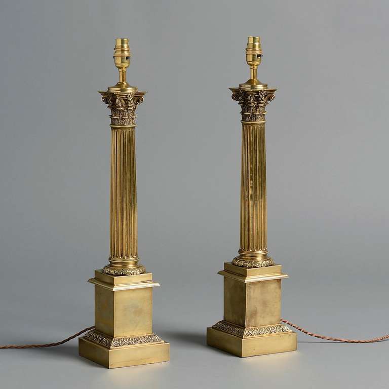 A PAIR OF LATE VICTORIAN BRASS CORINTHIAN COLUMN LAMPS, FITTED FOR ELECTRICITY, WITH ACORN WREATH SOCLES AND SQUARE LEAF-CAST PEDESTALS, circa 1875.