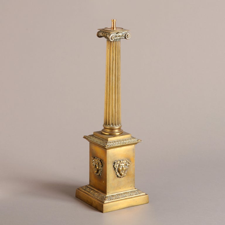 AN UNUSUAL LATE REGENCY BRASS IONIC COLUMN LAMP WITH SQUARE PEDESTAL APPLIED WITH BACCHIC MASKS, CIRCA 1820.