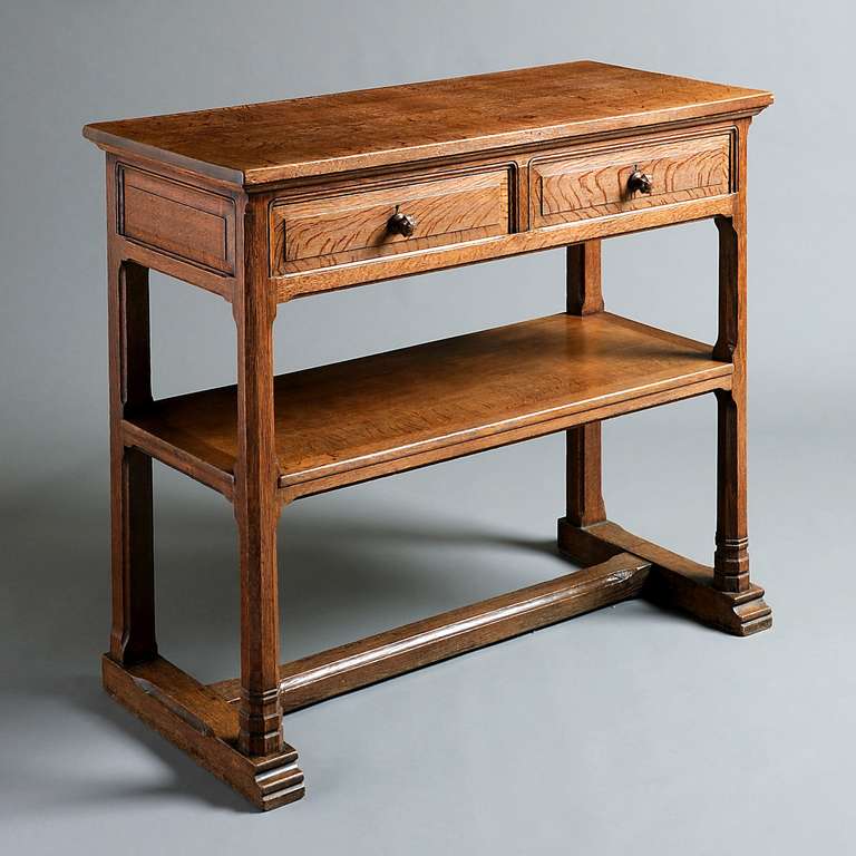 AN OAK SIDE TABLE DESIGNED BY SIR ROBERT LORIMER, CIRCA 1900.
The two paneled drawers with carved handles above an under tier on chamfered supports. 
