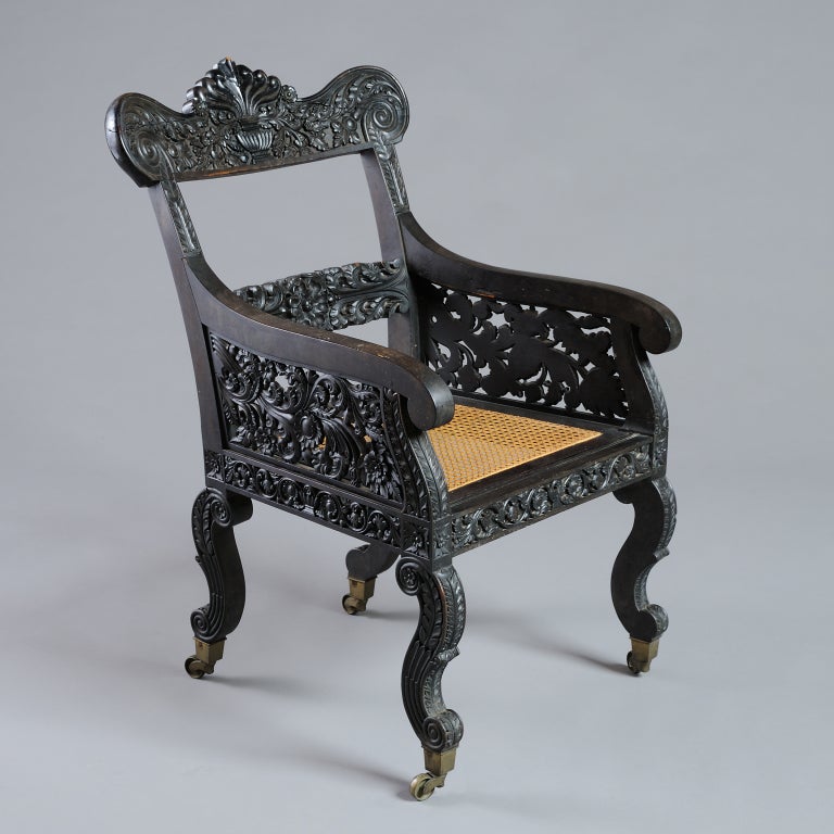 AN ANGLO-INDIAN CARVED EBONY ARMCHAIR ON S-SCROLL LEGS, CIRCA 1830.